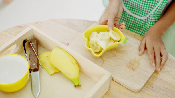 Elementary mixed girl eating banana at table, practical life skill activity in Montessori education school