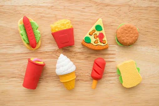 Flat lay of cute various fast food products and drinks eraser toy set on wooden background minimal style. Kid learning, development and funny play by small eraser toy in school accessories, food and drink concept.