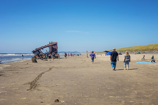 Warrenton, USA - August 8, 2023. People visit the Fort Stevens State Park beach on a hot summer day. The famous 1906 wreck of the Peter Iredale remnants attract tourists.