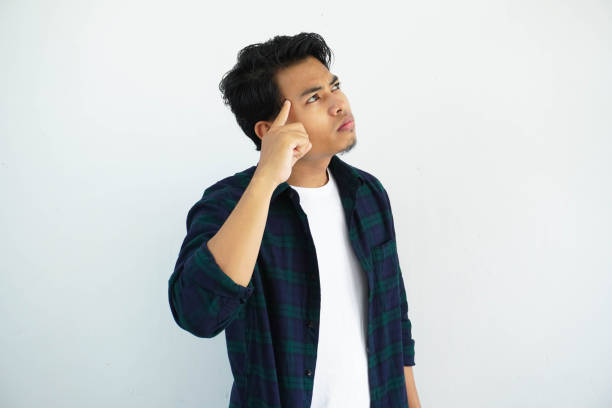 istock young asian man pointing finger to his head and showing thinking gesture isolated on white background. 1620075443