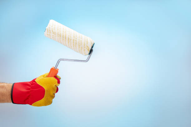 istock hand in gloves holding roller brush on blue background with place for text. Home improvement, DIY concept. 1620077282