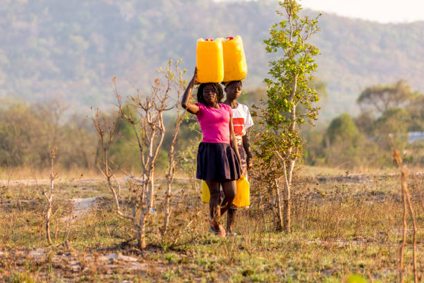 물이 부족한 지역에서 갤런의 물을 머리에 이고 있는 두 소녀 - developing countries 이미지 뉴스 사진 이미지