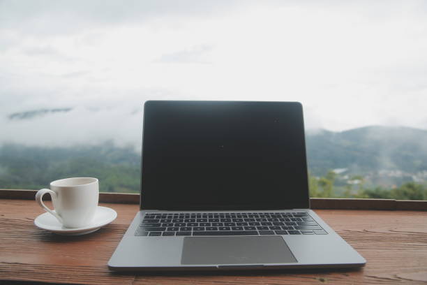 istock Computer Monitor, Keyboard, coffee cup and Mouse with Blank is on the work table at the sky mountain river and trees front view background. 1620199733