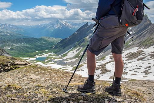 legs of a hiker wearing short and hiking shoes standing at the top of mountain with beautiful alpine landscape