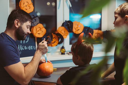 Children with father carving a traditional Jack lantern from pumpkin. Halloween concept. Image with selective focus