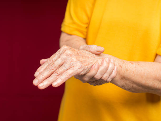 istock Senior woman suffering from wrist pain while standing against a red background 1620238426