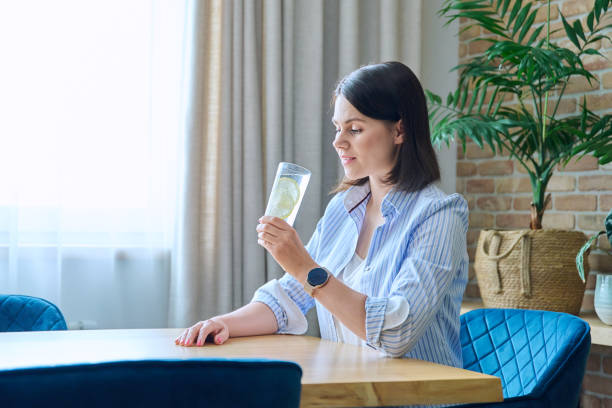 istock Young woman drinking water with lemon, sitting at the table 1620265933