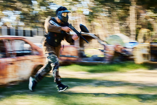Paintball, blurry action or man running in shooting game with speed or fast motion on fun battlefield. Mission focus, moving or war soldier with gun for survival in competition in nature or forest