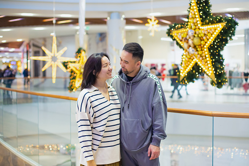young Asian Kazakh couple, man and woman look at each other with love in Christmas shopping mall. newlyweds, young family. portrait