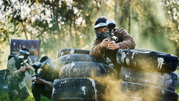 team, paintball and tires for cover bunker or protection while firing or aiming down sights together in nature. group of people waiting in teamwork for opportunity to attack or shoot in extreme sport - paintballing violence exercising sport imagens e fotografias de stock