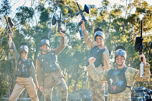 Team, paintball and portrait in celebration for winning, victory or achievement on the battlefield together in nature. Group of paintballers enjoying win, success or teamwork with guns in the air