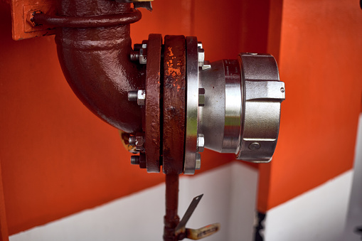 Standard flange connection in oil and gas, shipping industry for fuel oil bunkering manifold on orange, metal wall.