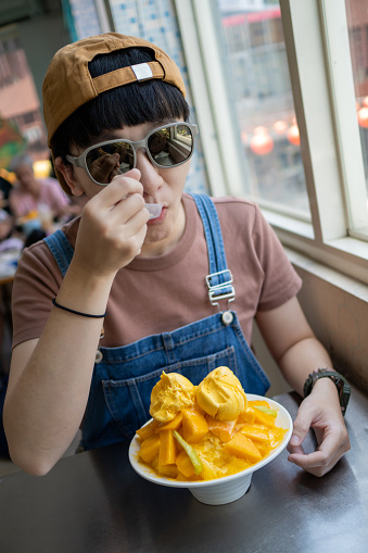 The young woman eats mango ice refreshingly during summer travel, which is quite refreshing and thirst-quenching.