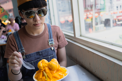 The young woman eats mango ice refreshingly during summer travel, which is quite refreshing and thirst-quenching.