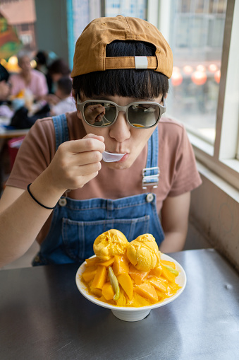 The young woman eats mango ice refreshingly during summer travel, which is quite refreshing and thirst-quenching.