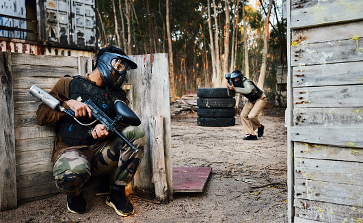 Sports, paintball and man with gun for battle, game or competition outdoors on field. War, military camouflage and male soldier with weapon on shooting range to hide from player in exercise fight.