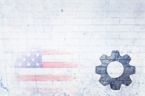 Messy grungy White Bricks wall pattern with grunge texture with a a grey machinery wheel spare part and faed USA flag. Apt for use as posters, backdrops, banners, greeting cards for US Labor day, May day.