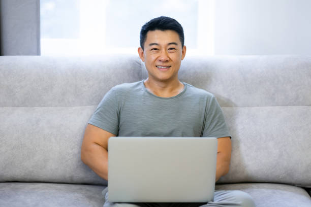 istock Smiling man sits on a comfortable sofa in the living room, relaxes while working on a laptop. 1620397826