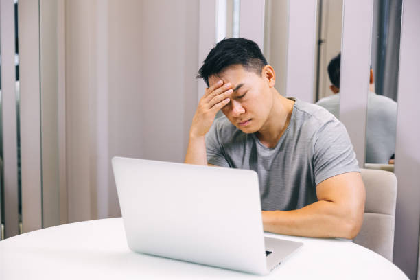 istock Young tired manager sitting at home with laptop computer having tired look holding his hand on head having pain closing his eyes being sleepy and exhausted. Tiredness 1620398368