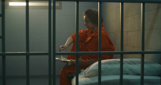 Prisoner gives dinner from food serving trolley to female criminal Prisoner in orange uniform gives dinner from food serving trolley to female criminal in prison cell. Woman criminal sits on the bed, serves imprisonment term for crime in jail or detention center. prison meal stock pictures, royalty-free photos & images