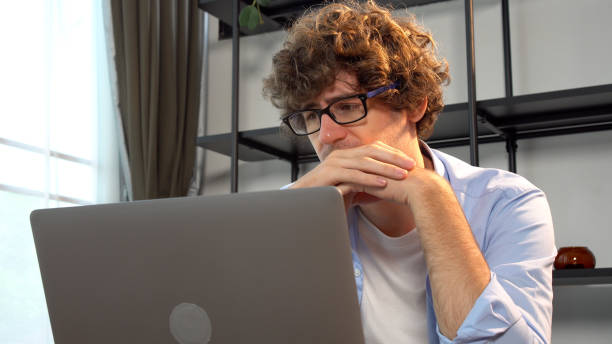 istock Serious young man wear eyeglasses thinking worry problems something in room. Thoughtful unhappy casual male eyewear looking laptop think about plan job in workplace at home. Lifestyle difficulty. 1620423167