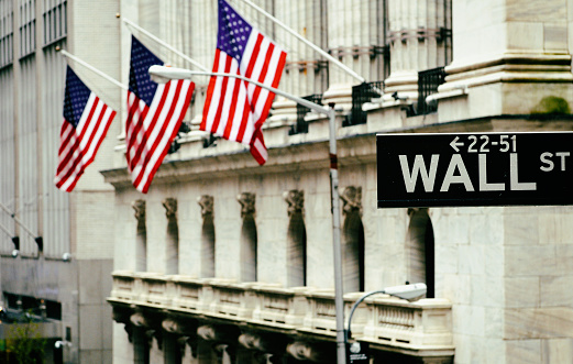 Wall Street sign with american flags and New York Stock Exchange in Manhattan, New York City, USA.