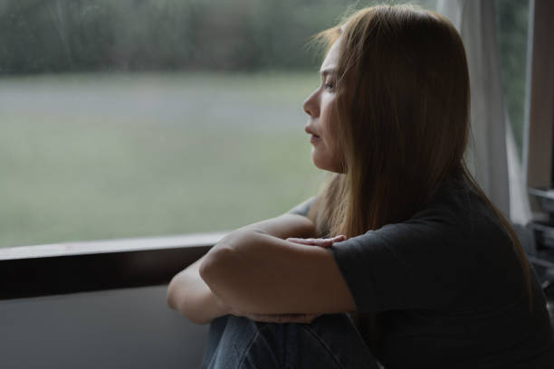 istock Depressed woman sitting by a large window with sad emotion on her face expression 1620434818