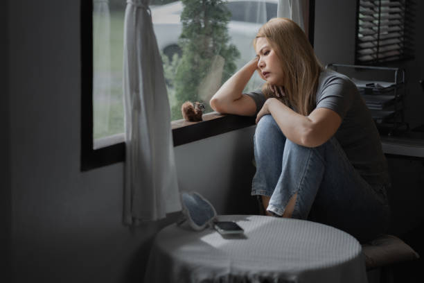 istock Depressed woman sitting by a large window with sad emotion on her face expression 1620434820