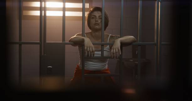 istock Female prisoner stands in jail cell, looks at camera 1620450542