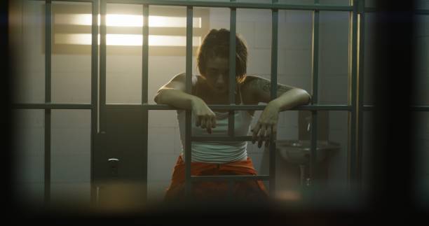istock Female prisoner stands in jail cell, looks at camera 1620453682