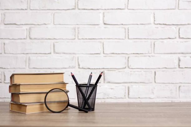istock stack of books, pencils and magnifying glass on the table in office or library, copy space over white brick wall background 1620461229