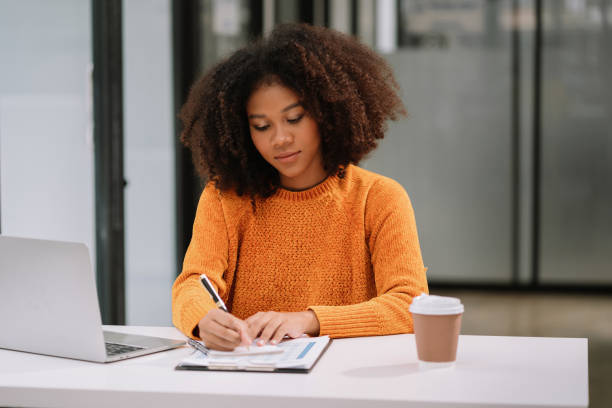 istock Business woman using laptop to work and writing on notebook with pen in office with mobile next to laptop. 1620461992