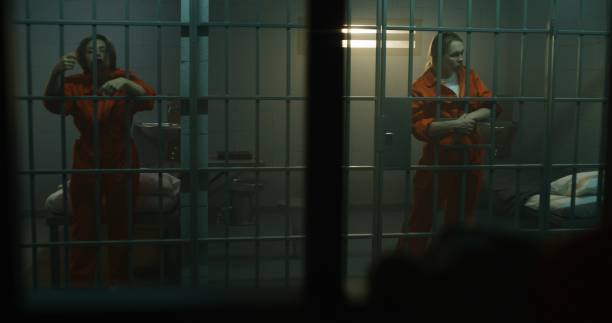 istock Two female prisoners stand and walk behind bars in jail cell 1620468174