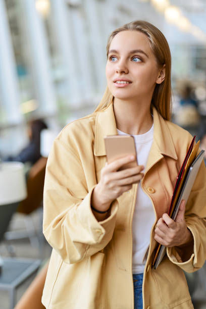 istock Happy girl student using mobile phone looking away walking indoors. 1620472019