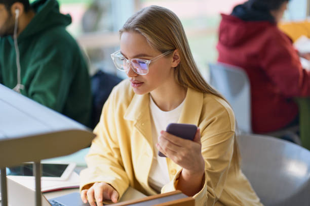 istock Girl student using mobile phone looking at laptop sitting at desk in university. 1620472585