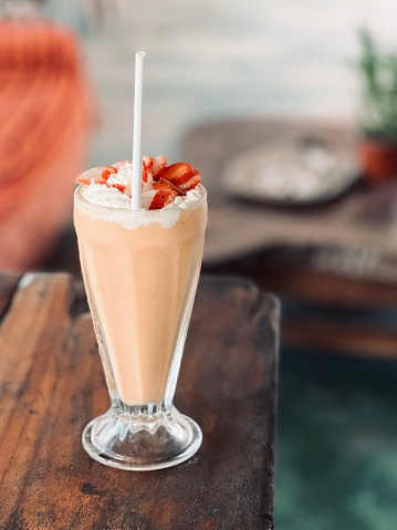 A clear glass cup filled to the brim with fresh strawberry milkshake on a wooden table