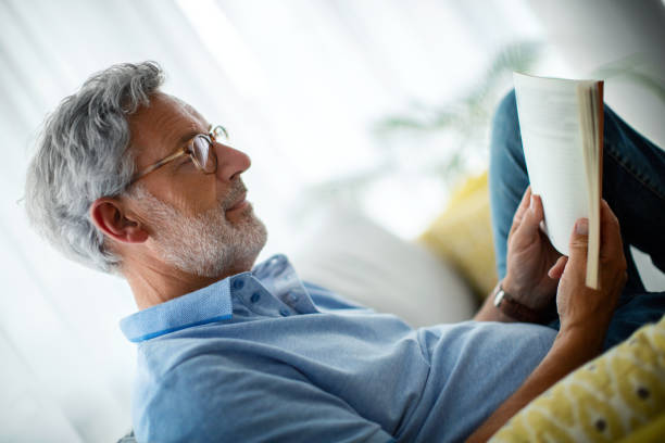 istock Mature man reading a book on the sofa. 1620475277