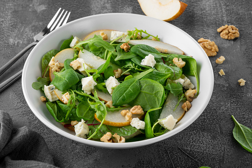 Salad with spinach, arugula, fresh pear, nuts and gorgonzola cheese with olive oil in a bowl. Healthy food concept