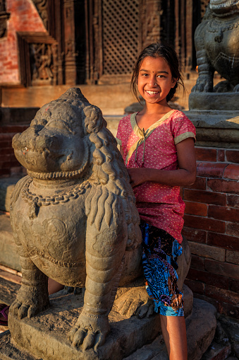 Nepali young girl posing on an ancient Hindu temple in Bhaktapur. Bhaktapur is an ancient town in the Kathmandu Valley and is listed as a World Heritage Site by UNESCO for its rich culture, temples, and wood, metal and stone artwork.