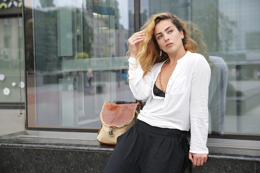 Woman leans against the window of a mall and straightens her hair