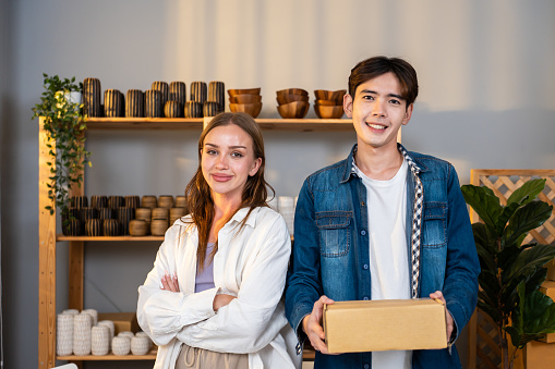 Portrait young man and woman check vase order on shelf for customer. Beautiful attractive business people work to preparing parcel boxes checking ecommerce shipping online retail to sell at home store