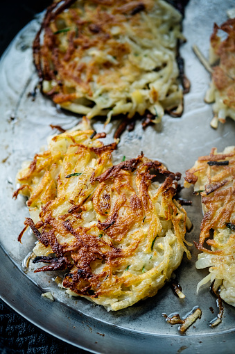 Frying latkes or potato cakes. These are made with, grated potato, white onion, egg, flour and some creamed horseradish sauce. Then the individual cakes are shallow fried in sunflower oil. It is important to strain as much water out of the potatoes as possible. Colour, vertical format with some copy space.
