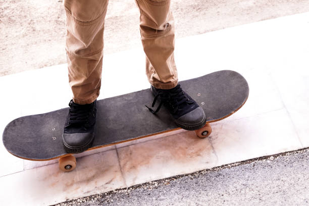Low section of a skater leaning against a brick wall with their skateboard propped up beside them, showcasing urban street style and skateboarding culture