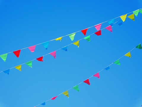 Colorful celebration with multi-colored flags and buntings hanging under clear sky.