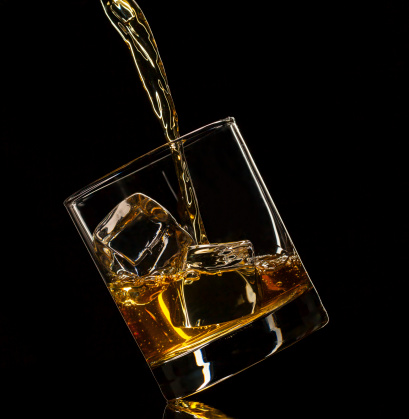 Isolated shot of whiskey pouring into glass on black background