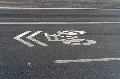 On the asphalt of the city painted with white paint the sign indicating the direction of travel in a bike lane.