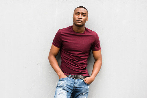 Portrait handsome young African American man leaning against gray wall and staring