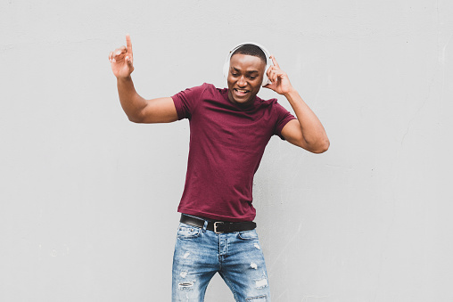 Portrait happy African american man listening to music with headphones and dancing by gray background