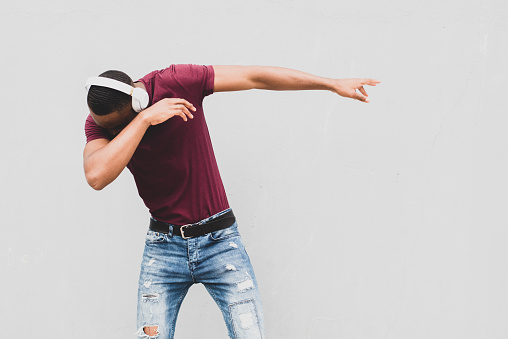 Portrait African american man enjoying music with headphones and dancing by gray background