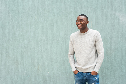 Portrait happy African american man standing with hands in pocket by green wall